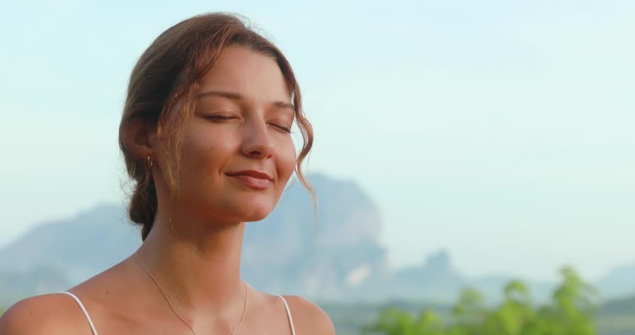 Close-up of a serene woman with eyes closed practicing breathing meditation in a lush tropical landscape with mountains. Ideal promo for wellness, mindfulness, breathwork, or healing content.