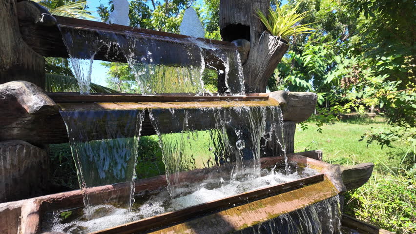 Serene Outdoor Water Feature Showcasing Cascading Water Over Wooden Tiers, Surrounded by Lush Greenery, Evoking Tranquility and Peace for Nature Lovers
