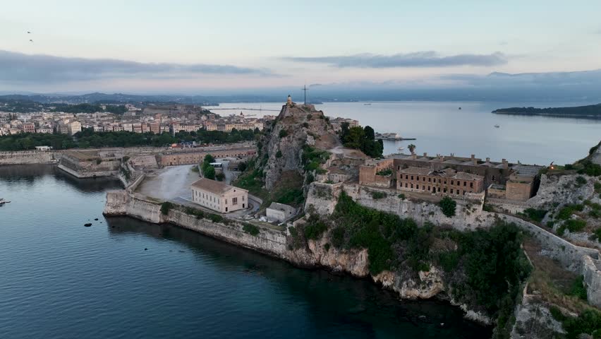 Breathtaking aerial footage of the Old Fortress in Corfu, Greece, at dawn, featuring the lighthouse on top and the town waking up under a soft, morning sky overlooking the sea