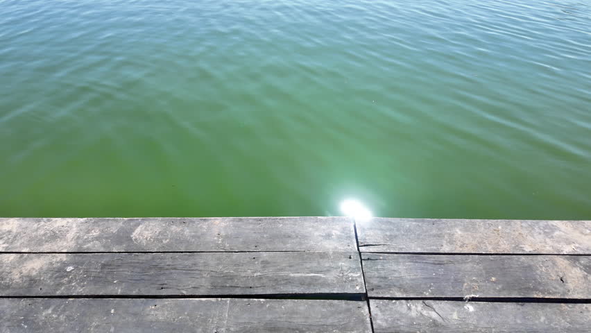 Serene Wooden Dock Over Calm Green Water Reflecting Sunlight, Inviting Tranquility and Connection to Nature in Peaceful Outdoor Atmosphere Perfect for Relaxation and Contemplation