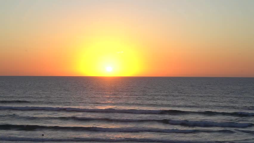 Fast time-lapse of a sunset over the sea, with rolling waves in the foreground as the sun rapidly descends toward the horizon. The scene captures dramatic light changes, flowing water movement, and the calming rhythm of the ocean at dusk.