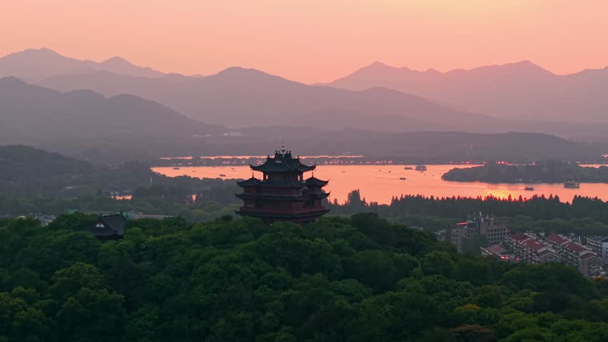 Aerial view of Chenghuang pagoda at sunset over Xihu lake in Hangzhou featuring mountains and lush green trees