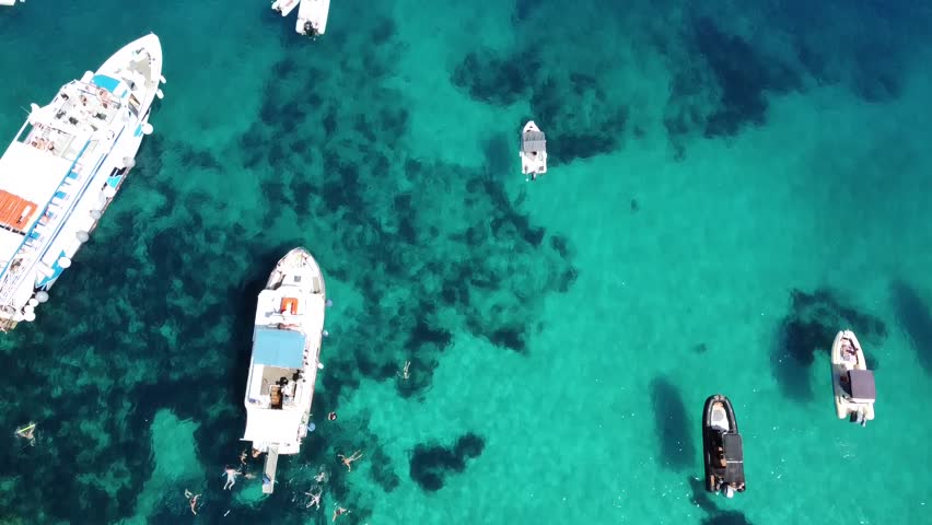 Aerial Drone View Two Tourist Boats Passing Each Other Blue Lagoon Sivota Greece - Top Down Footage of White Water Trails Behind Moving Vessels in Turquoise Ionian Sea, Anchored Yachts and Swimmers in Crystal Clear Mediterranean Water, Transport Boats Bringing Tourists to Remote Paradise Coast, Dynamic Forward Movement Drone Shot of Marine Traffic in Azure Bay, Cinematic Travel Video of Greek Island Summer Tourism Activity, Boat Wake Foam Trails in Pristine Turquoise Lagoon, Active Coastal Scene with Multiple Boats and People Swimming, Overhead View of Nautical Transportation in Secluded Cove, Summer Vacation Travel Destination Footage Perfect for Tourism Marketing Holiday Promotion Marine Transportation Documentary, Authentic Greek Island Life with Traditional Tourist Boats Operating in Calm Bay Waters, Real Time Action of Maritime Activity in Mediterranean Paradise, Professional Drone Cinematography for Travel Agency Promotion Yacht Charter Advertising Tourism Board Campaigns Social Media Content, Relaxing Summer Vibes Video Background Showing Peaceful Coastal Life and Marine Movement in Epirus Coast