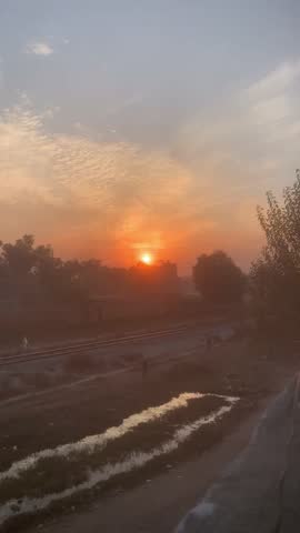 Vibrant sunset over rural landscape with railroad tracks and water reflection.