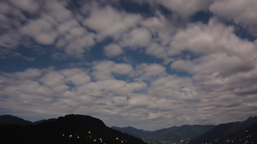 Beautiful white clouds passing over Himalayan mountains with stars and night sky in the background. Time lapse movie of cloud cape, Sikkim, India.