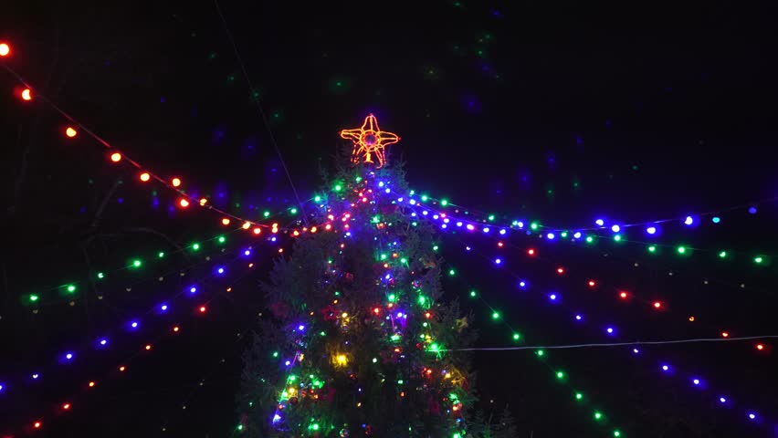 Festive Christmas tree decorated with sparkling colorful garlands with a red star against the background of the night sky