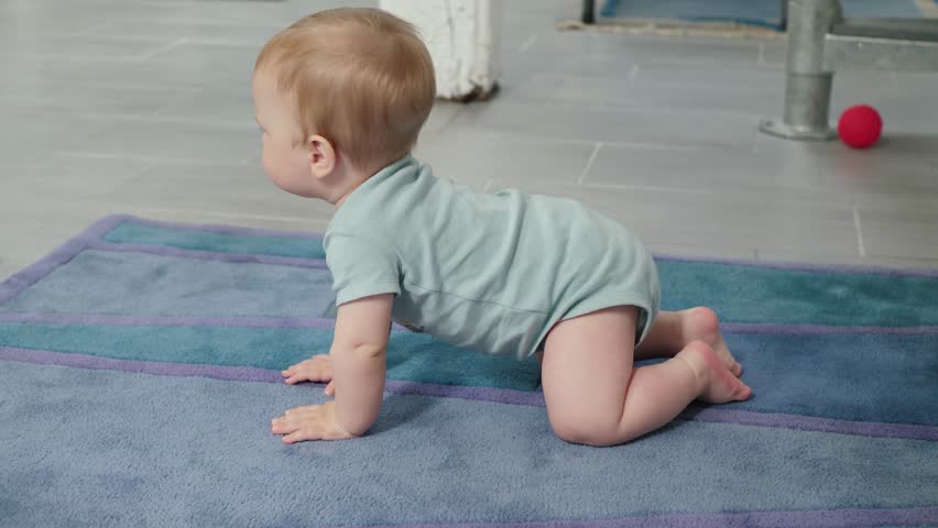 The baby crawls on a soft carpet, symbolizing the development of the first movements and the curiosity of infants exploring their bright world