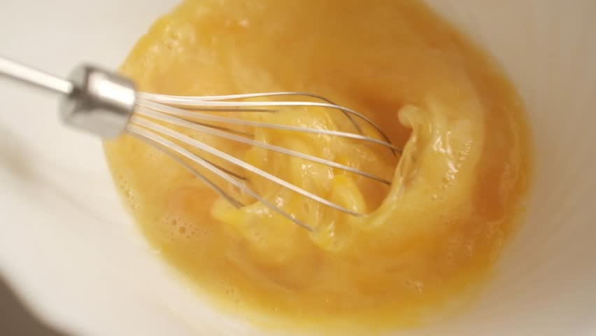 Closeup slow motion video of uncooked raw eggs. Whisking eggs for an omelette, scrambled eggs, baking, egg dishes. Preparing food, home cooking, cooking process.