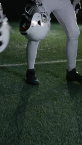 Vertical shot of American football team players lifting up helmets while standing in circle on pitch and cheering, for team building motivation and unity before championship match