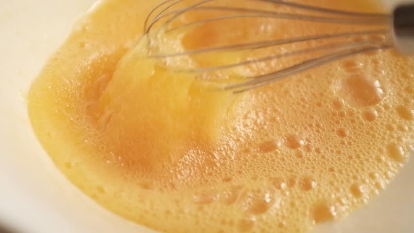 Closeup slow motion video of uncooked raw eggs. Whisking eggs for an omelette, scrambled eggs, baking, egg dishes. Preparing food, home cooking, cooking process.