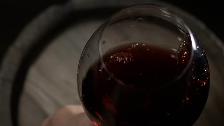 Pouring red wine into a glass at a rustic wine tasting event in a cozy cellar during the evening
