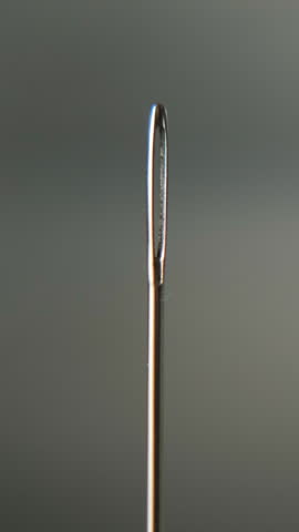 Vertical video. Macro shot of hand carefully threading white thread through the small eye of a sewing needle, representing precision, patience and handmade craft concept