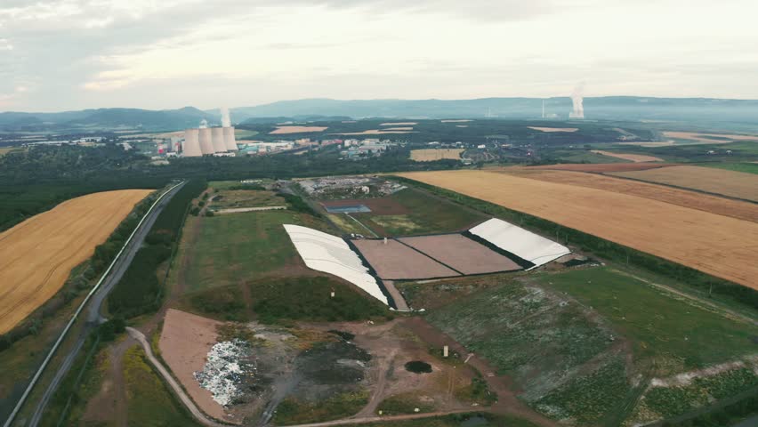 High-quality footage of landfill with flyover geomembrane, drone cruising, nature surrounding energy plant chimneys, showcasing environmental themes 4k