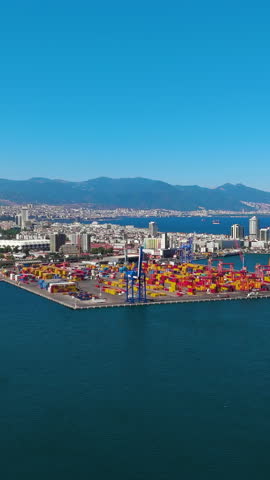 Vertical video. Izmir, Turkey. Container yard and large cranes at Izmir Port for commercial freight operations in Aegean Sea on sunny day. Aerial view. Rich colors