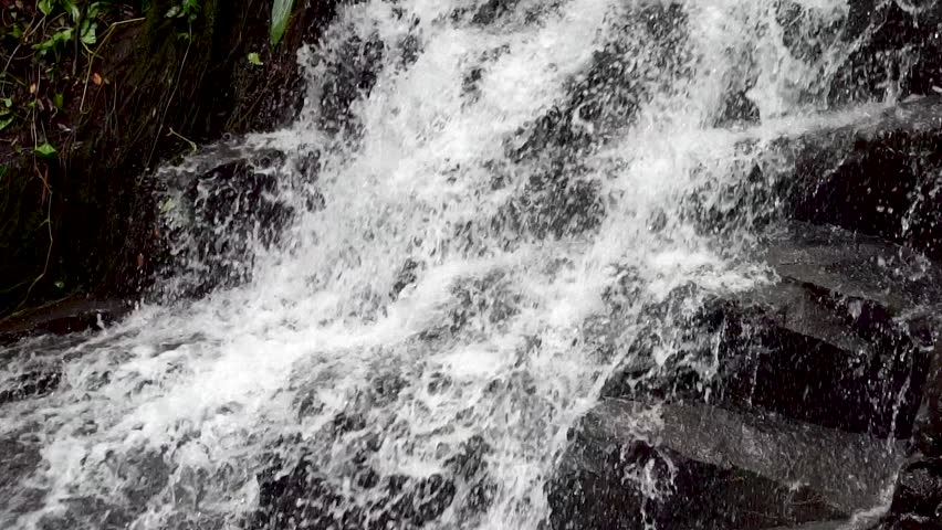 Close up slow motion of raging fresh water cascading down dark rock face. Nature background of waterfall splashing on wet stones in the forest. High frame rate 120fps.
