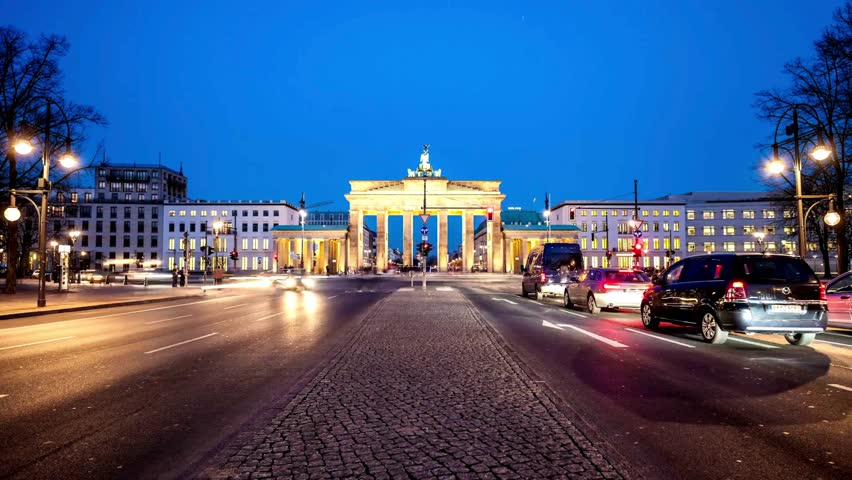 Illuminated Brandenburg Gate stands prominently against a night skyline of Berlin. Cars and pedestrians move briskly, highlighting vibrant city life and historic significance.