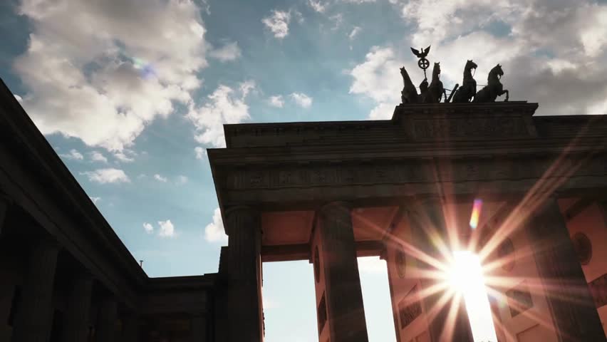 The sun sets behind the iconic Brandenburg Gate, illuminating the grand structure and creating a breathtaking silhouette against a colorful sky.
