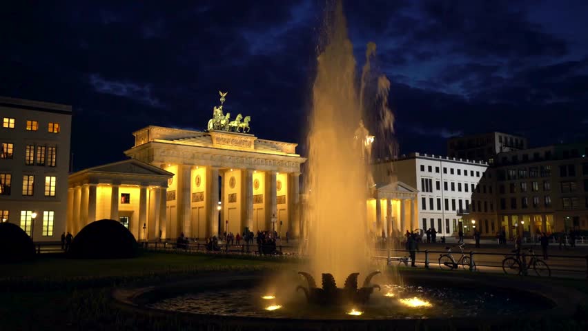 The iconic Brandenburg Gate stands majestically under the night sky, with a vibrant fountain in the foreground, creating a captivating atmosphere in Berlin.