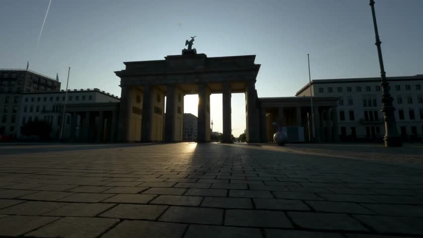 Brandenburg Gate stands majestically in Berlin as sunlight creates a stunning silhouette, casting warm rays across the cobblestone plaza during golden hour.