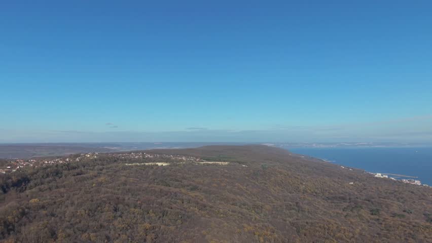 Aerial view of coastal city skyline overlooking calm blue sea, urban shoreline landscape, modern buildings meeting nature from above.