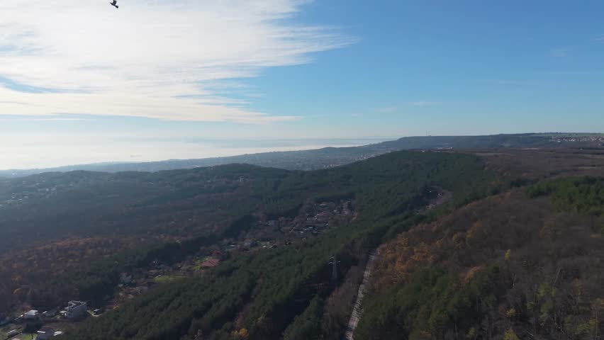 Aerial drone panorama over forested hills and small town, distant horizon, calm atmosphere, natural landscape stretching into the distance.