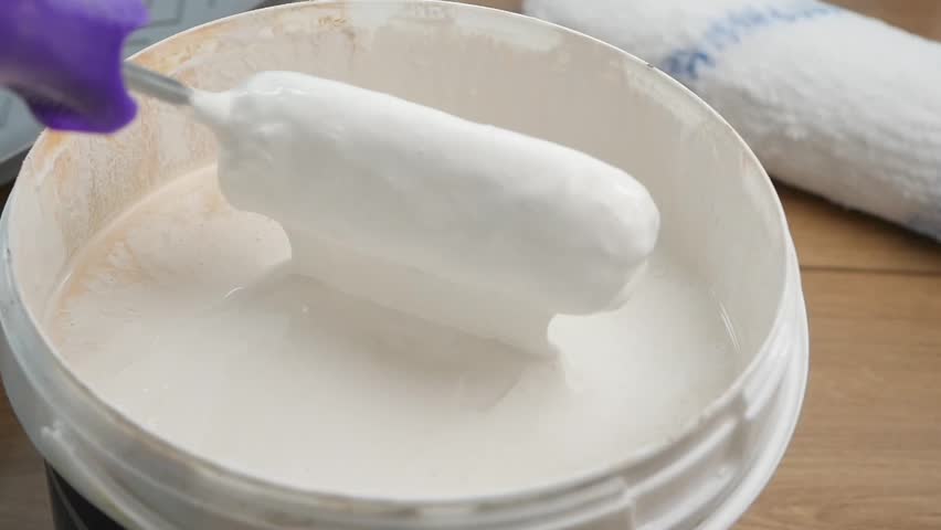 Painting a wall with a roller and white paint in a cozy room