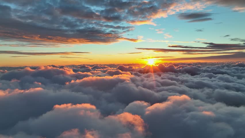 Sunrise above clouds shows bright colors and changing light in the early morning sky. Epic sunset over the clouds. Warm sun sets over the horizon in clouds