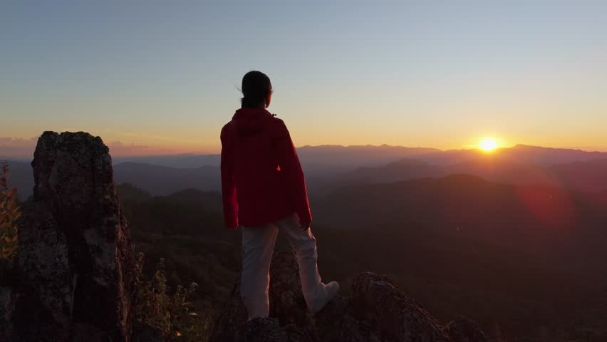 Silhouette of a person feeling strong and empowered, standing tall on the top of a mountain at sunrise