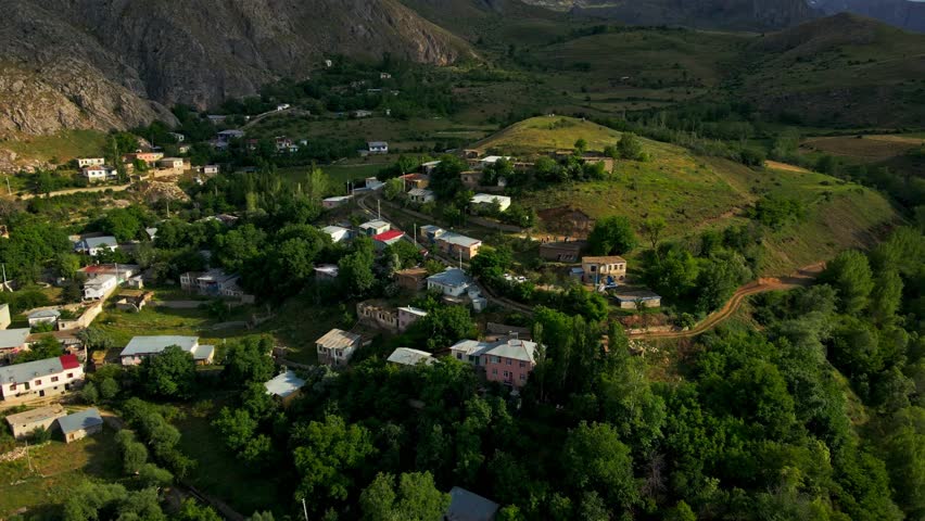 A small town with houses and trees in the background. The town is surrounded by mountains, giving it a peaceful and serene atmosphere. The houses are spread out
