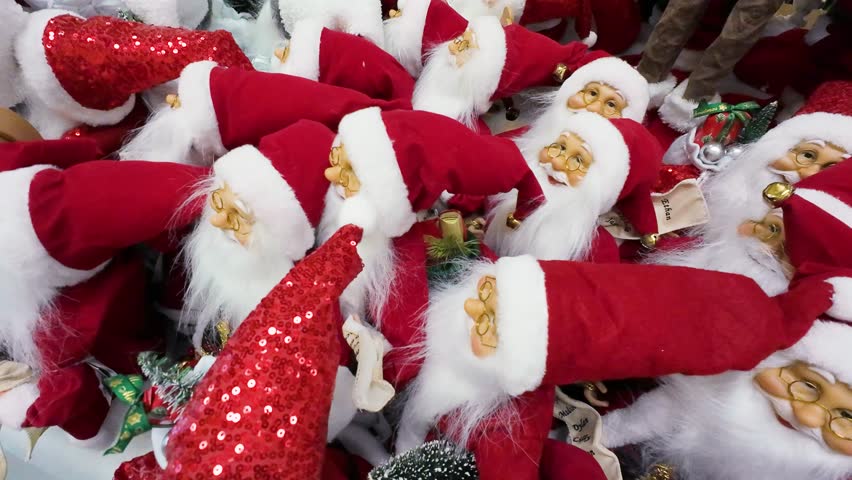 Close-up shot of many Santa Claus toys on display in a shopping center. Festive Christmas decorations for sale in a retail store. Holiday season shopping for traditional Santa figures.