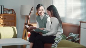 Happy young asian women sitting on a sofa and studying together. Cheerful female friends enjoying a relaxing time at home, reading and talking - Powered by Shutterstock - Get 15% off with code: PIKWIZARD15