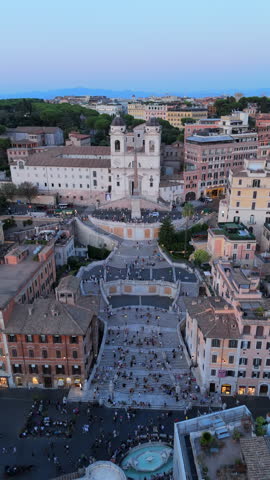 Cinematic High angle drone city view captures Rome Italy rooftops and Spanish Steps area with historic buildings, busy streets and dense urban texture under calm evening sky.
