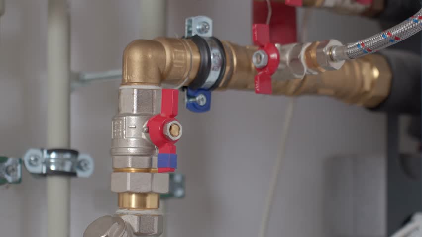 Close-up of technician hand adjusting valve on heat pump piping system with pipes and fittings. Concept of heating maintenance and plumbing service