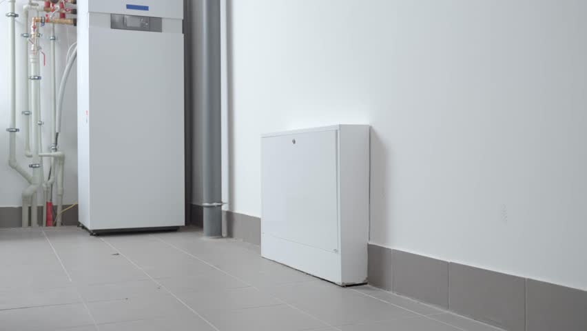 Technician inspecting underfloor heating manifold with pipes and valves in utility room. Concept of heating installation, plumbing maintenance, HVAC service and residential energy system