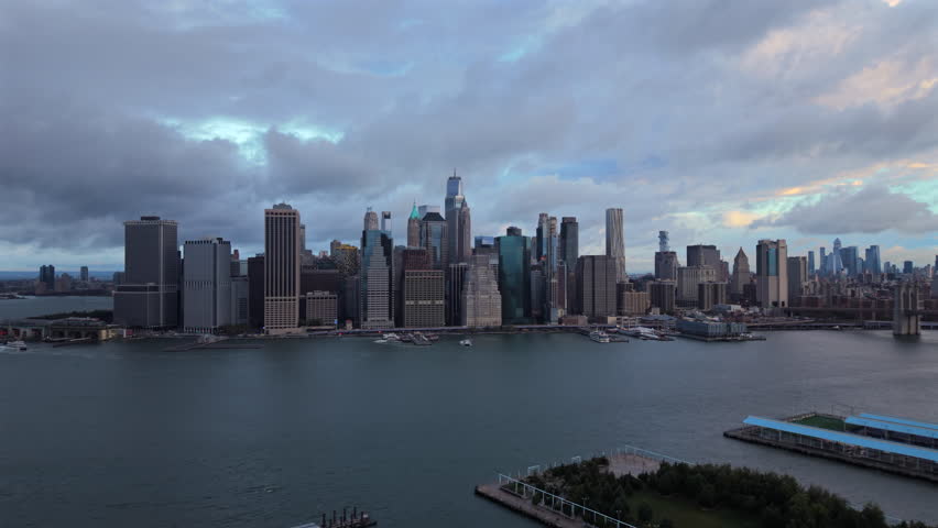 Morning Aerial drone scene of New York City, New York showing tall downtown towers, open river water and dramatic textured clouds forming a bright wide skyline atmosphere. USA