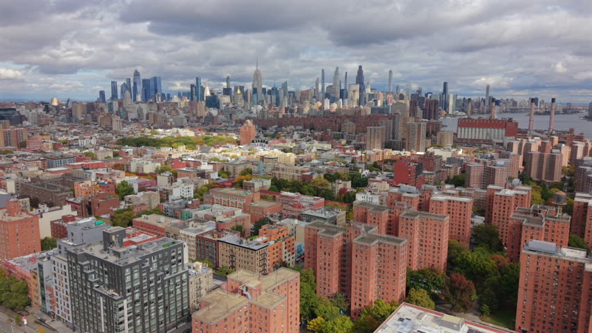 Wide aerial view showing dense residential buildings and urban blocks with Manhattan skyline in background. City architecture, everyday neighborhoods and modern skyline of New York City, New York.