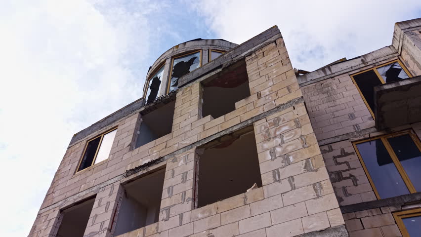 Vacant structure looms under a gray sky, its shattered windows revealing fragments of a forgotten past. Nature begins to reclaim the space, hinting at stories untold.