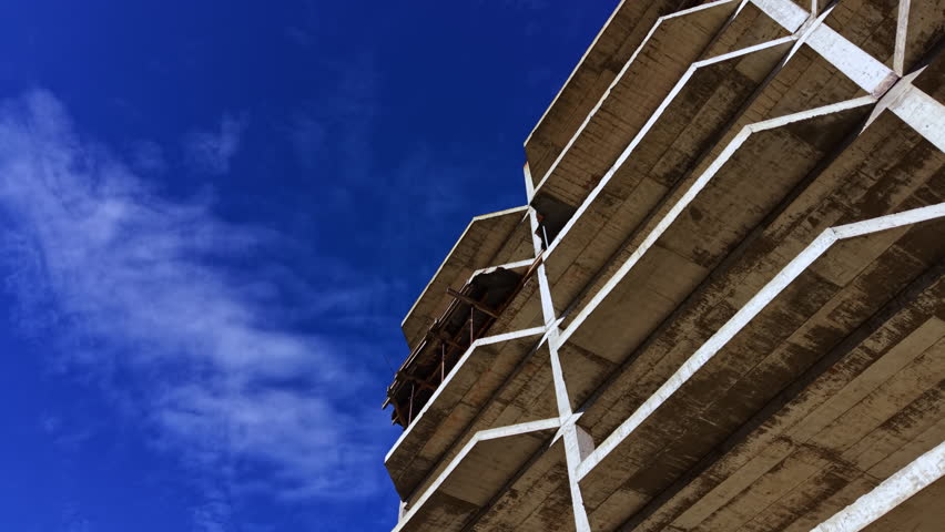 Massive concrete structure rises prominently, showcasing industrial beauty. The clear sky adds depth, highlighting the rawness of construction work taking place under the sun.