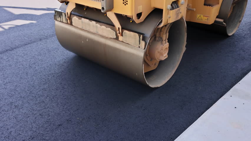Yellow steamroller machine is flattening fresh asphalt at construction site