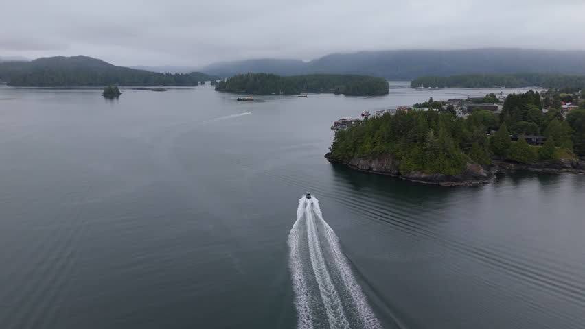 Drone following small boat on ocean near rocky coast with mountains and forest