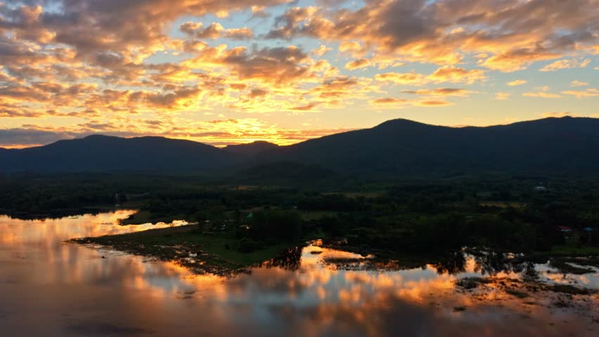  A time-lapse image of golden clouds drifting over a lake, a beautiful sunset over a tranquil lake, with mountains reflected in the colorful sky.
