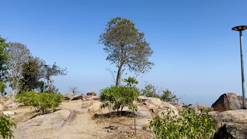 Slow panoramic shot from rocky mountain viewpoint over valley farmland and distant reservoir under clear sky