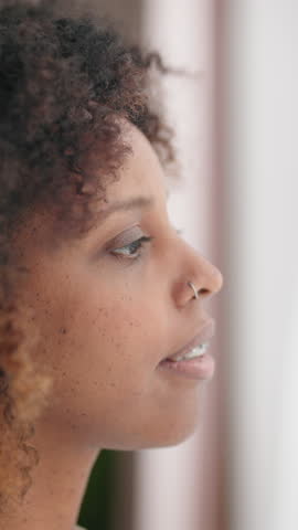 Beautiful african woman looking at window and waiting someone, portrait indoors. Joyful black lady standing alone in home window with white curtain, female guest of modern luxury hotel, closeup shot