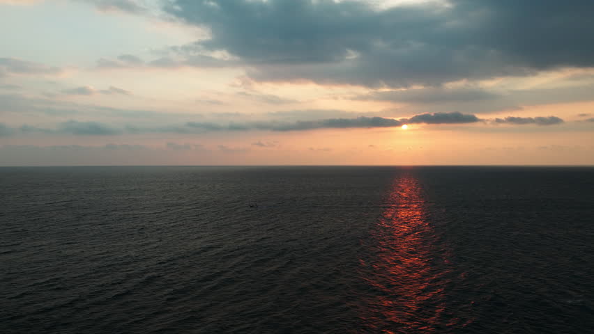 A fishing boat sails through shimmering waters at sunset, casting long shadows over the Indian Ocean. A peaceful aerial view of Sri Lanka
