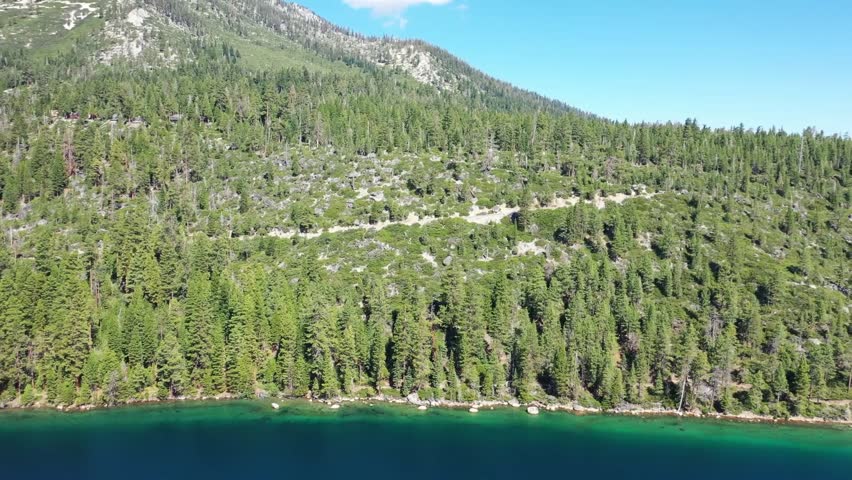 Panning shot across Emerald Bay at lake Tahoe on a sunny day. Bright green highlights in the water along the edge of the lake with lake Tahoe in the background.