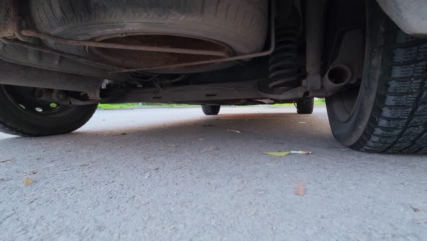 POV drive video from an action camera mounted under a car, showing undercarriage, wheels and suspension moving over a wet road. Dynamic automotive motion, speed, vehicle mechanics and transportation