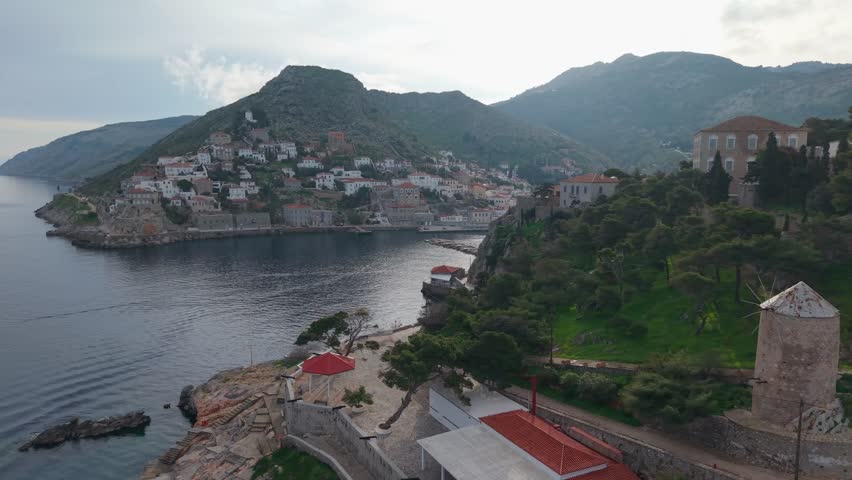 A morning drone orbit reveals Hydra’s harbor and its traditional village architecture bathed in soft early light.