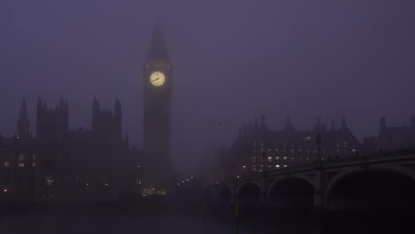 Atmospheric scene of Big Ben and Parliament emerging from dense fog over the Thames with Westminster Bridge on a dark, gloomy London day in diffused light.