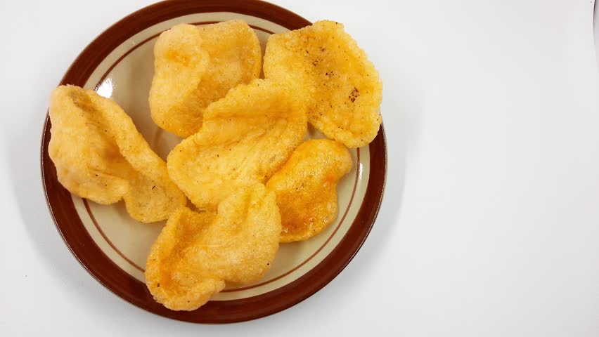 Fried shrimp crackers known as krupuk are presented piled on a simple brown and cream ceramic plate against a clean white background ready to eat.