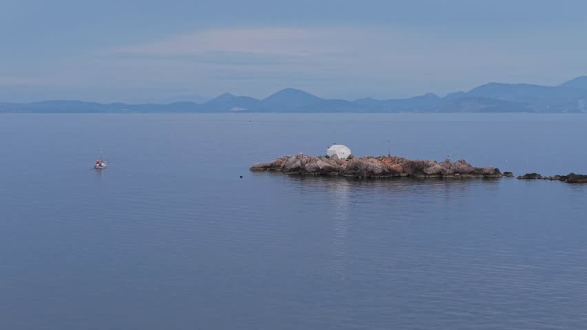 A winter morning drone capture of Hydra island, showing the iconic taxi boat used for transportation gliding smoothly across the calm sea near the harbor.